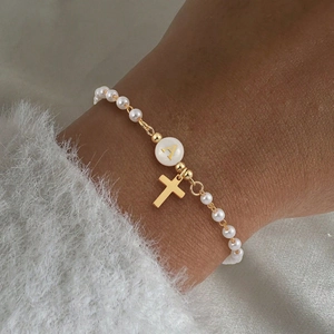 Gros plan d'un bracelet en perles avec croix dorée et breloque lettre A sur le poignet
