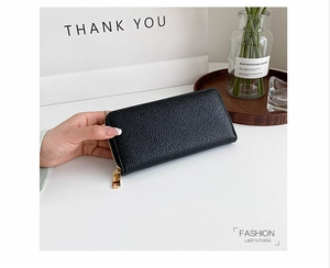 Close-up of elegant black pebbled leather long purse with gold zipper held in hand