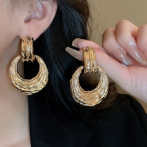 Detailed view of large gold textured metal hoop earrings with lava-style surface finish
