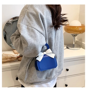 Rear view of a model wearing a mini blue crossbody bag with a large white bow decoration
