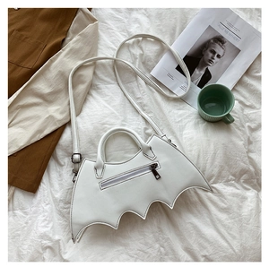 Detail of white bat-shaped PU leather bag with top handle and detachable strap on a bed