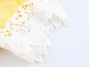 Detail of white lace embroidery on yellow fabric edge with intricate floral patterns