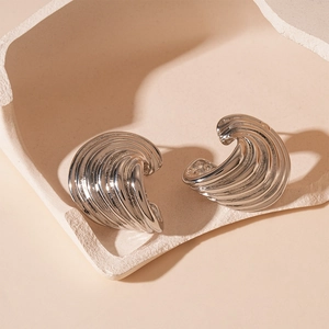 Macro view of silver C-shape metal earrings with textured wavy relief pattern