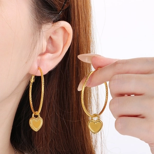Elegant gold twisted hoop earrings with heart charms shown on a model for a stylish look