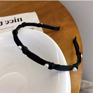 Elegant black satin headband with white pearls on a minimalist white ceramic bowl