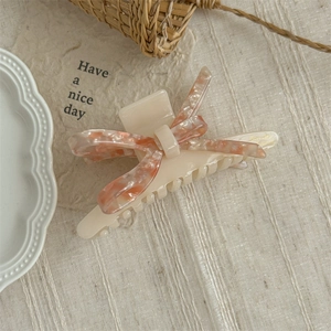 Detail of a cream acetate hair claw clip with a pink and white marble pattern bow