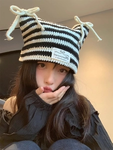 Detail of knit cat-ear beanie with black and white stripes and a white bow accent