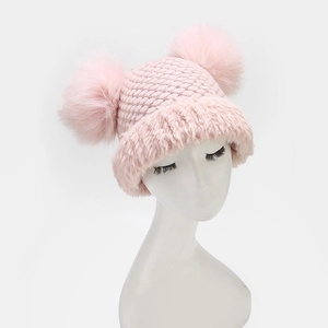 Close-up of pink winter knit hat featuring dual fox fur pom-poms and plush earflaps