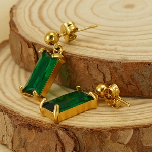 Close-up of gold 18K plated earrings with rectangle green zircon on natural wood