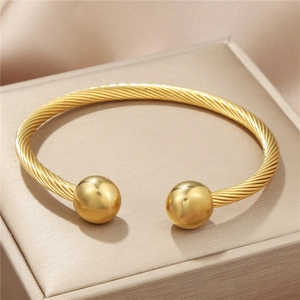 Detail of golden stainless steel cable cuff bangle with polished spherical ball ends