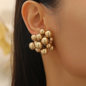 Close-up of a model wearing golden geometric bead cluster earrings with a high-shine finish