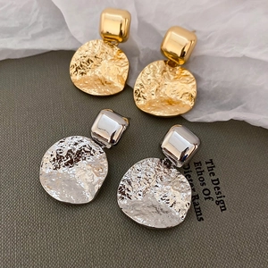Detailed view of square and hammered round gold and silver earrings on textured fabric