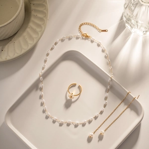Flat lay of gold necklace, ring and earrings set with white pearls in a ceramic tray