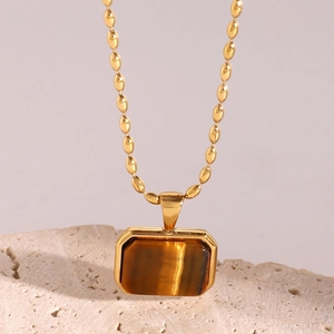 Close-up of golden bead chain necklace with rectangular tiger eye stone on stone