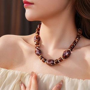 Dettaglio della collana con perle marroni marmorizzate e distanziatori dorati