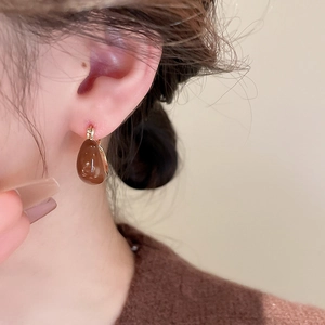 Détail d'une boucle d'oreille goutte en émail marron caramel portée par un mannequin