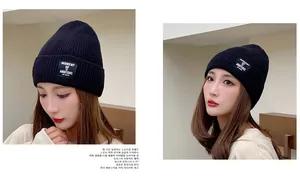 Detail of black ribbed knit beanie featuring an embroidered 'MOMENT OF AMBITIONS' patch