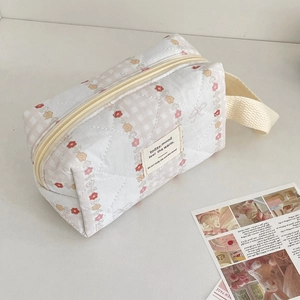 Detail of quilted makeup bag with red floral pattern, beige zipper, and side handle strap