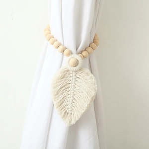 Detail of wooden beads and cotton leaf tassel tieback on white curtain fabric