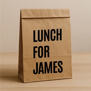 Close-up of brown kraft paper lunch bag with custom James text on wooden surface
