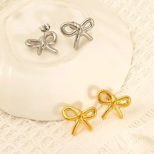 Golden and silver bow-knot stainless steel earrings on a decorative ceramic tray