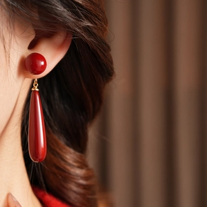Macro shot of long red teardrop resin earrings with gold metallic links worn by model