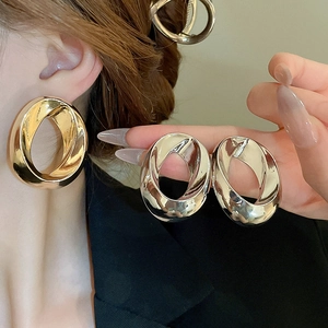 Close-up of stylish twisted oval drop earrings in polished gold and silver metallic finish