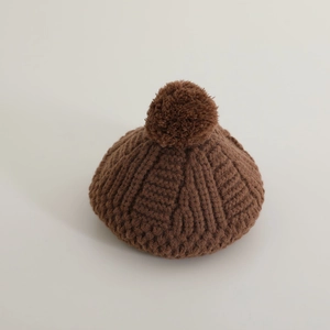 Détail de la béret en maille marron foncé avec texture épaisse et pompon sur le dessus