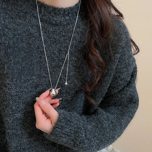 Detail of silver water-drop pendant on a long chain over a grey knit sweater