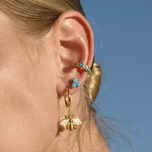 Golden bee pendant earrings set with turquoise stones worn by a model on sky background