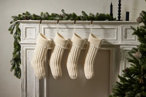 Detail of four cream-white knitted Christmas stockings hanging on a vintage white fireplace