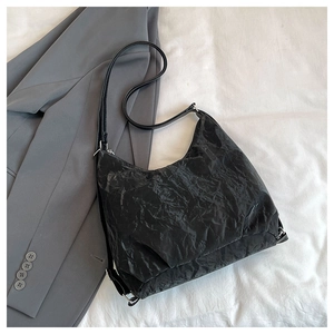 Detail of black wrinkled texture crossbody bag resting on a gray business blazer