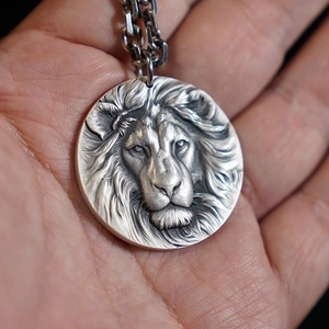 Detailed close-up of a silver lion head relief pendant on a metallic chain necklace
