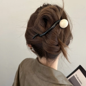 Pic à cheveux noir ondulé avec perle crème sur un chignon de cheveux bruns