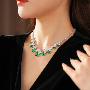 Gros plan d'un collier argenté avec des gemmes vertes en goutte d'eau et motif floral