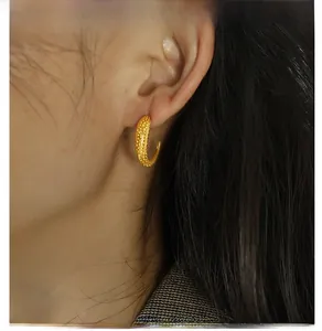 Close-up of textured golden C-shaped earring with caviar pattern on ear model