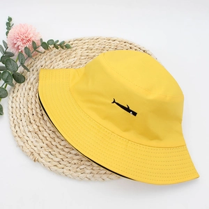 Yellow cotton bucket hat with black whale embroidery on a woven mat for summer sun protection