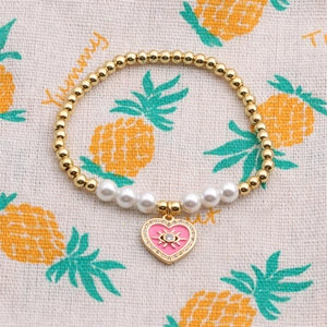 Dettaglio del bracciale con perle dorate e ciondolo a cuore rosa con occhio greco