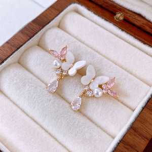 Detailed shot of gold butterfly earrings with pink zircon and pearls on a velvet display
