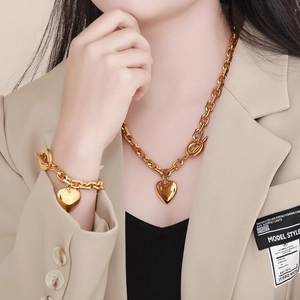 Close-up of a model wearing a golden heart pendant necklace and bracelet set in stainless steel