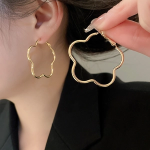 Macro view of a large gold flower shaped hoop earring worn to show polished metallic detail