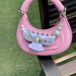 Purple heart hair claw clip attached to a pink handbag pearl chain on grass