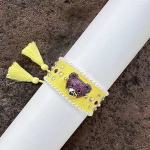 Macro detail of hand-woven yellow bracelet with purple crystal bear head and tassels