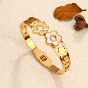 Golden cutout floral bangle with white enamel and crystal accents on a textured surface