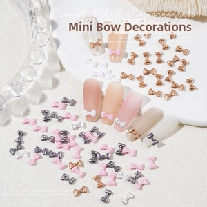 Detailed view of 3D mini bow nail charms in gold, silver, and pink on textured marble
