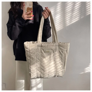 Detail of a soft beige quilted nylon tote bag with vertical stitching and brand patch