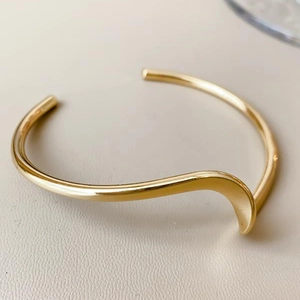 Minimalist gold tone wave shaped open cuff bracelet with polished metallic finish