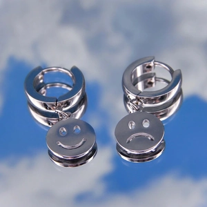 Unisex stainless steel hoop earrings with cutout smiley and sad face charms on sky reflection