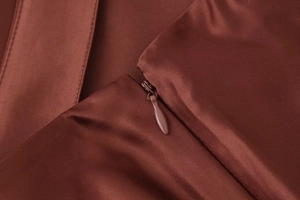Detailed macro view of invisible zipper closure on dark rust satin midi skirt fabric