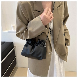 Detailed side view of a small black pleated cloud bag with silver chain strap on a model